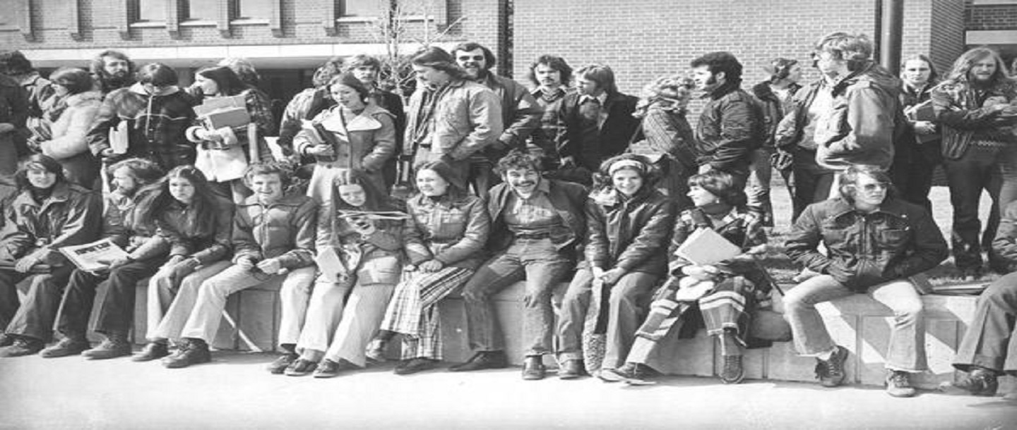 Students from Mankato State College sitting on wall in front of Armstrong Hall in the 1970s
